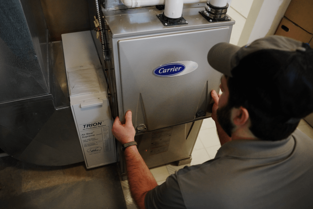 A Tyler Heating & Cooling employee inspecting a Carrier furnace in a customer's home