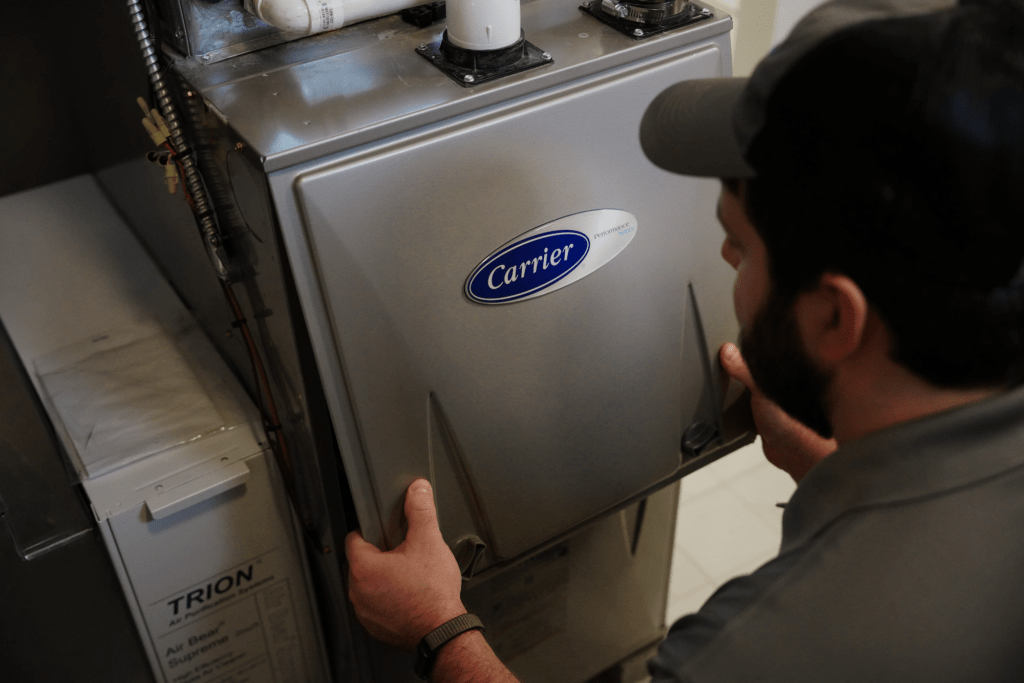 A Tyler Heating & Cooling employee removing the panel of a high-efficiency Carrier furnace
